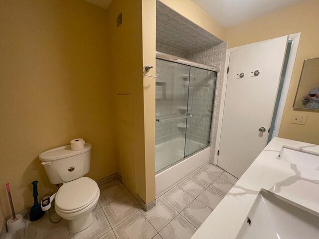 bathroom featuring toilet, bath / shower combo with glass door, vanity, and baseboards
