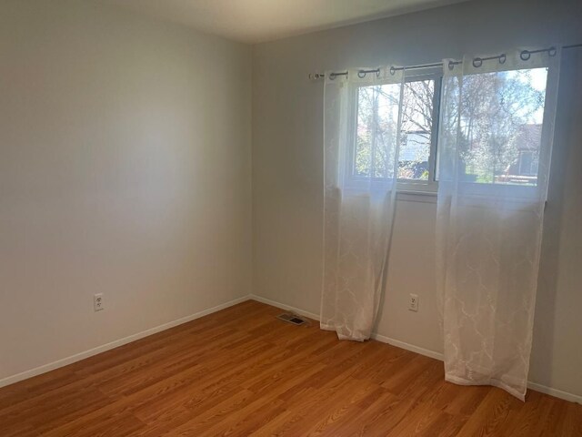 empty room with light wood-style floors, visible vents, and baseboards