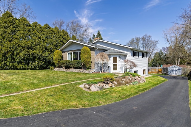 raised ranch featuring a storage shed, a front lawn, aphalt driveway, and an outdoor structure