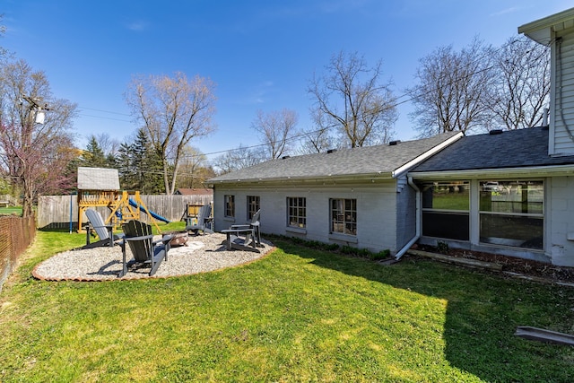 rear view of property with a fenced backyard, a fire pit, roof with shingles, and a playground