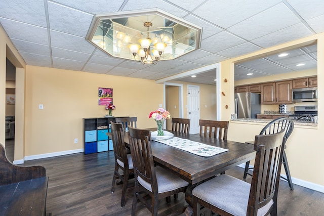 dining area featuring dark wood-type flooring, a drop ceiling, baseboards, and an inviting chandelier