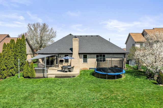 back of property featuring a chimney, brick siding, a trampoline, a yard, and a patio