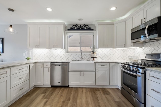 kitchen featuring white cabinets, a sink, light wood-type flooring, tasteful backsplash, and appliances with stainless steel finishes