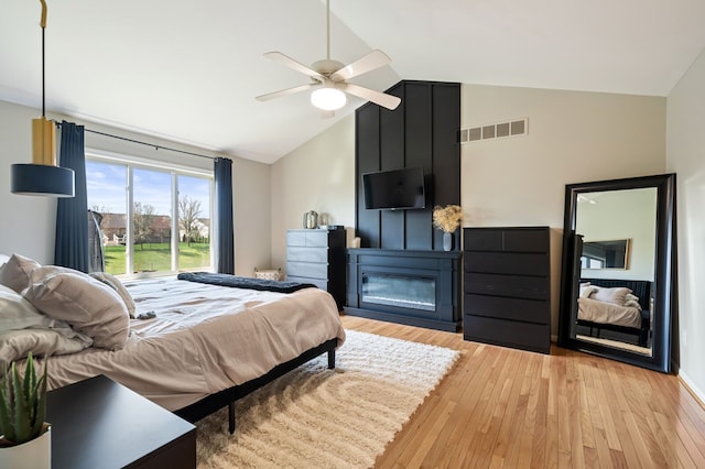 bedroom with lofted ceiling, visible vents, a large fireplace, and light wood-type flooring