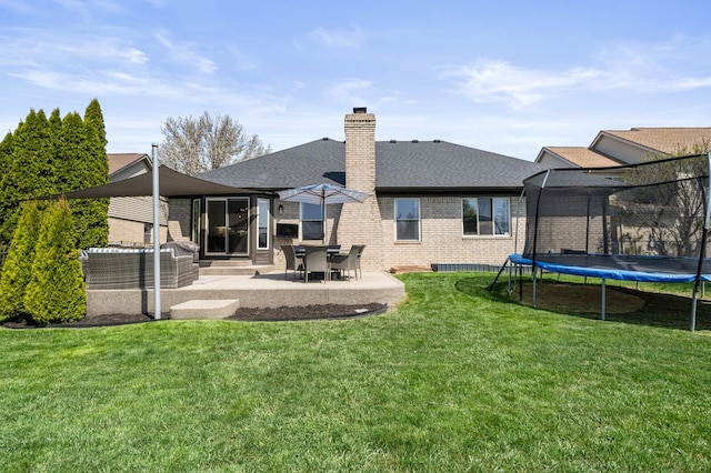 back of property with brick siding, a patio area, a trampoline, a chimney, and roof with shingles