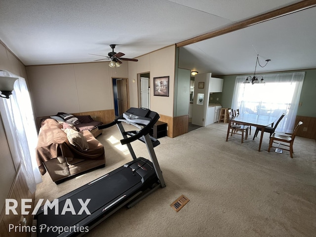 workout area with carpet flooring, visible vents, wainscoting, lofted ceiling, and ceiling fan with notable chandelier