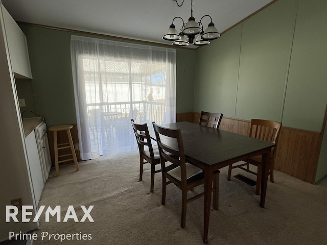 dining room featuring an inviting chandelier, a wainscoted wall, ornamental molding, and light carpet