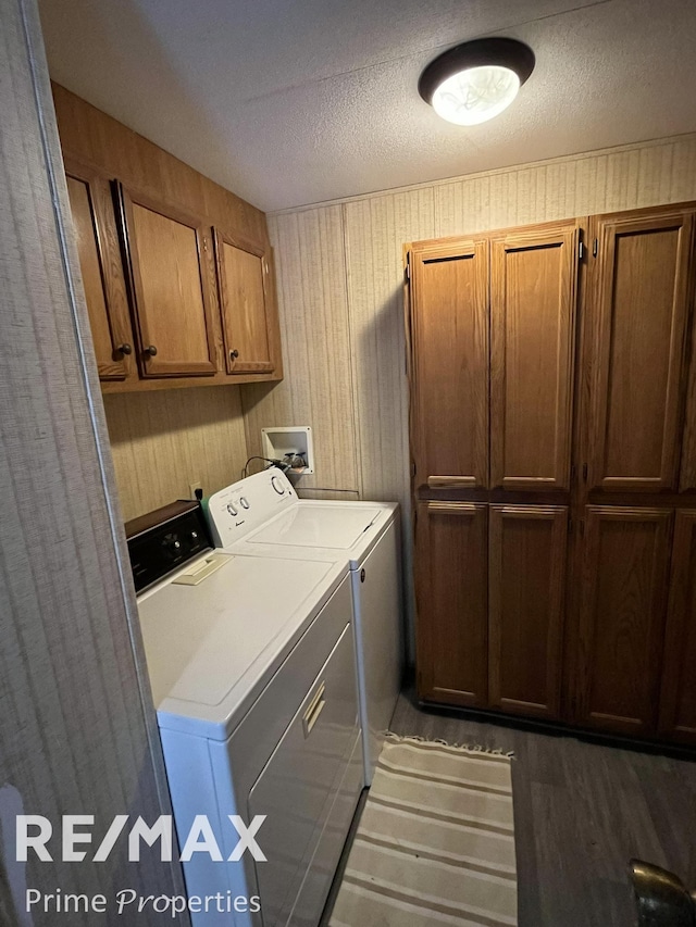 clothes washing area featuring a textured ceiling, cabinet space, wood finished floors, and washer and clothes dryer