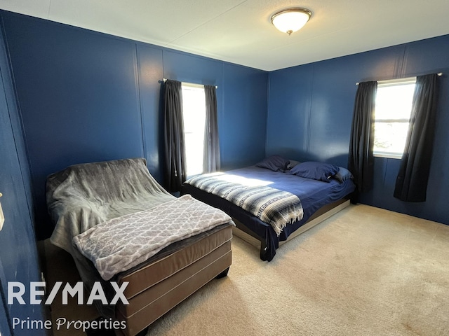 bedroom featuring light carpet and a decorative wall
