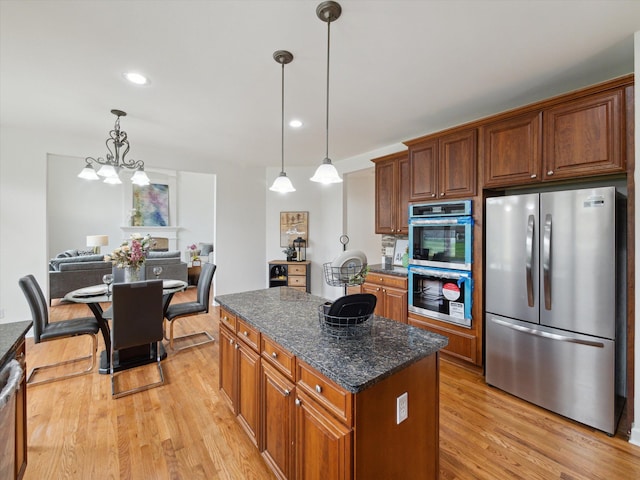 kitchen with dark stone counters, hanging light fixtures, stainless steel appliances, light wood finished floors, and a kitchen island