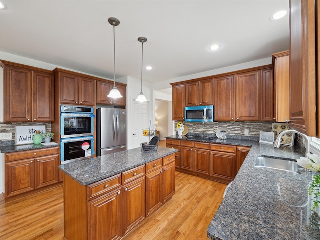 kitchen featuring a center island, a sink, light wood-type flooring, stainless steel appliances, and backsplash