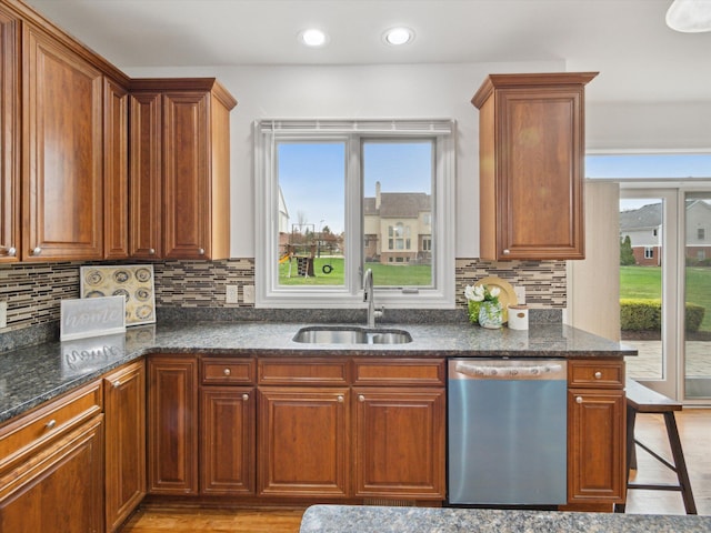 kitchen featuring stainless steel dishwasher, a sink, dark stone countertops, and light wood-style flooring