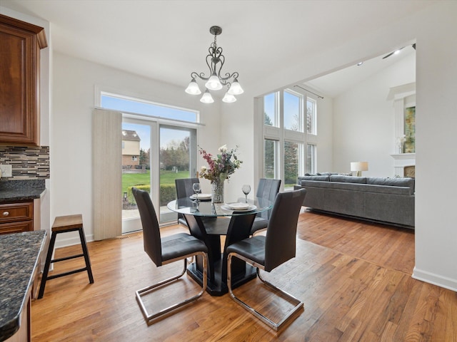 dining area with a wealth of natural light, an inviting chandelier, vaulted ceiling, and light wood-type flooring