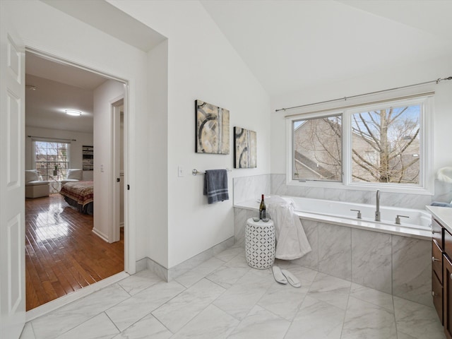 ensuite bathroom with a garden tub, vaulted ceiling, ensuite bathroom, marble finish floor, and baseboards