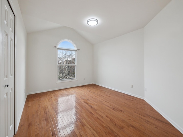 unfurnished bedroom with a closet, lofted ceiling, hardwood / wood-style floors, and baseboards