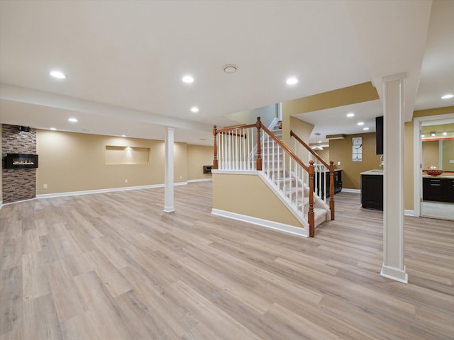 finished basement featuring stairway, light wood-style floors, a large fireplace, baseboards, and recessed lighting