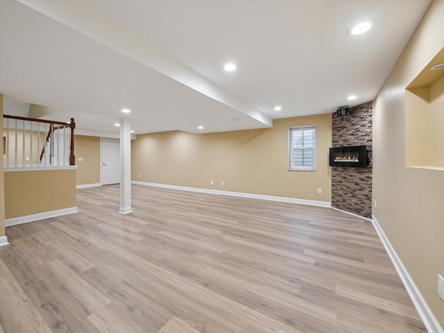 basement featuring light wood finished floors, baseboards, a fireplace, and stairs