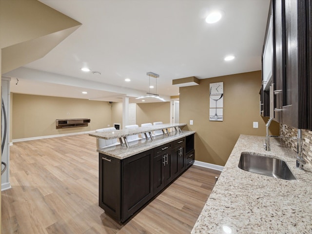 kitchen with light stone counters, a sink, light wood-style floors, baseboards, and open floor plan
