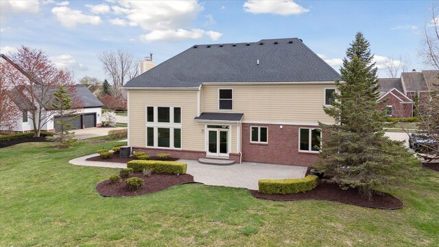 back of property featuring a chimney, brick siding, a garage, a lawn, and a patio