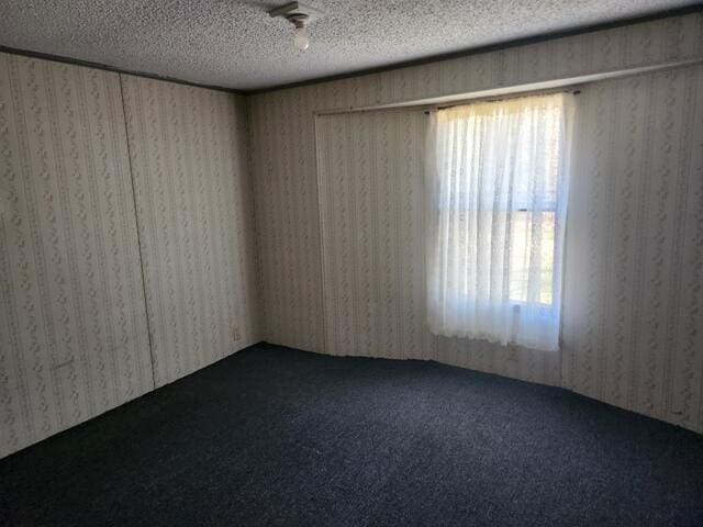 empty room with dark carpet, a textured ceiling, and wallpapered walls