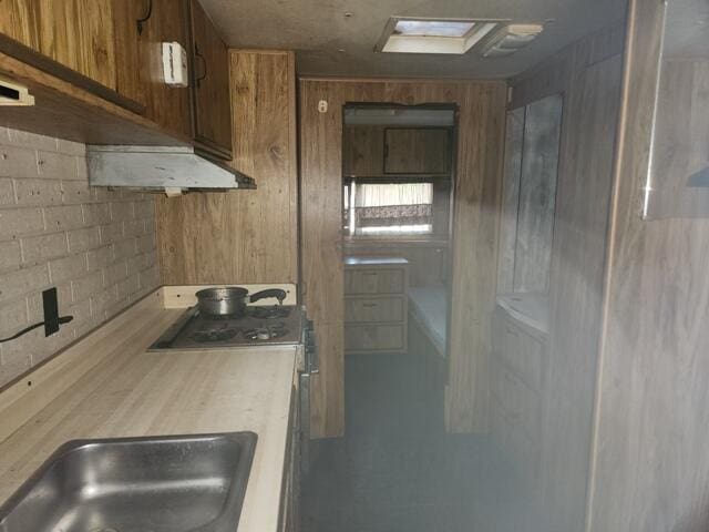 kitchen featuring light countertops, wooden walls, range with gas cooktop, a sink, and brown cabinetry