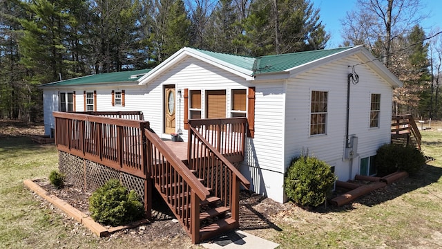 rear view of property featuring metal roof, a lawn, a wooden deck, and stairway