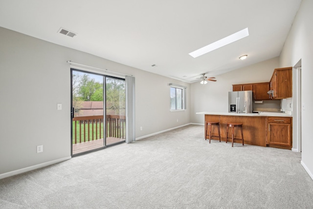 kitchen with stainless steel fridge with ice dispenser, a skylight, a kitchen bar, light carpet, and vaulted ceiling