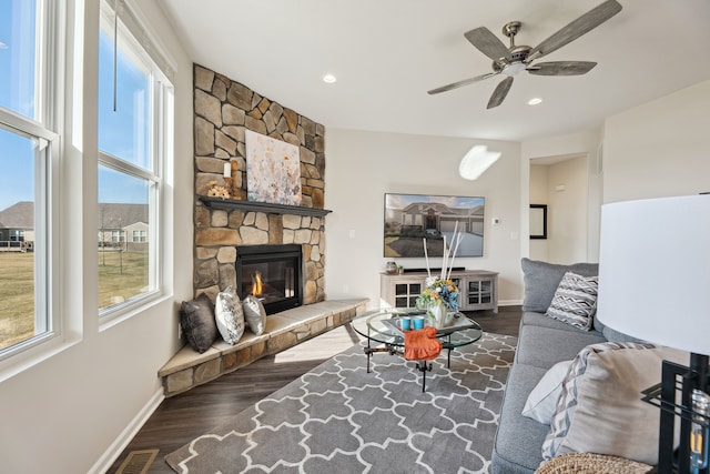 living room with wood finished floors, visible vents, a ceiling fan, a stone fireplace, and baseboards