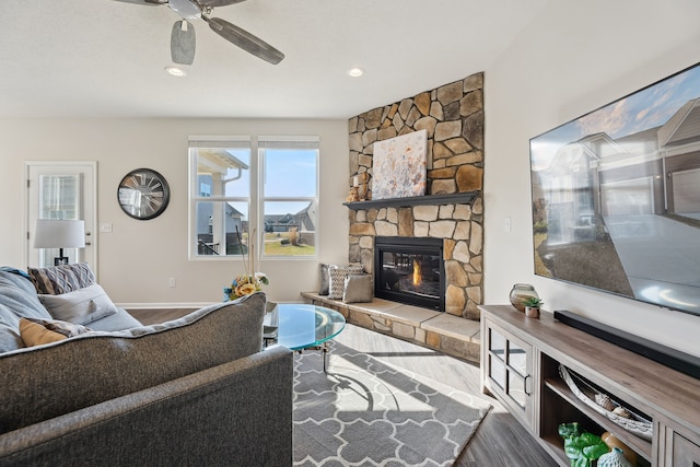 living room with baseboards, a ceiling fan, wood finished floors, and a stone fireplace