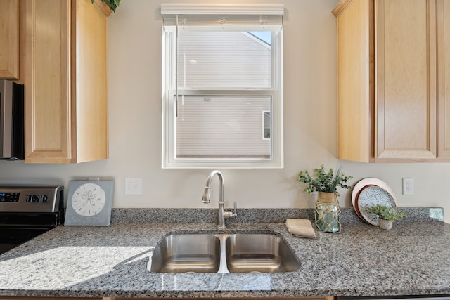 kitchen with light stone counters, stainless steel range with electric stovetop, light brown cabinetry, and a sink