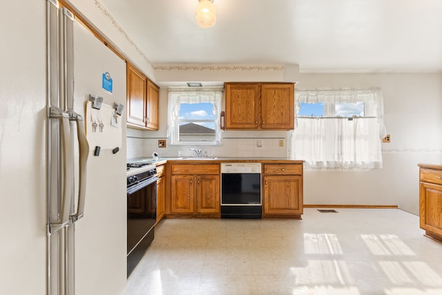kitchen with gas stove, freestanding refrigerator, brown cabinetry, dishwasher, and a sink