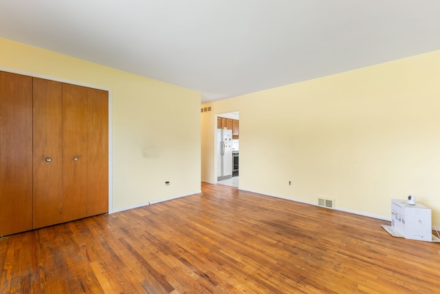 unfurnished bedroom with wood finished floors, visible vents, freestanding refrigerator, and a closet