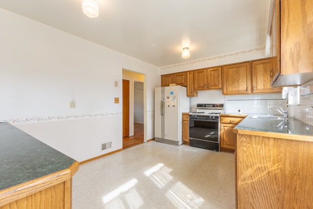 kitchen with a sink, freestanding refrigerator, gas range, and light floors