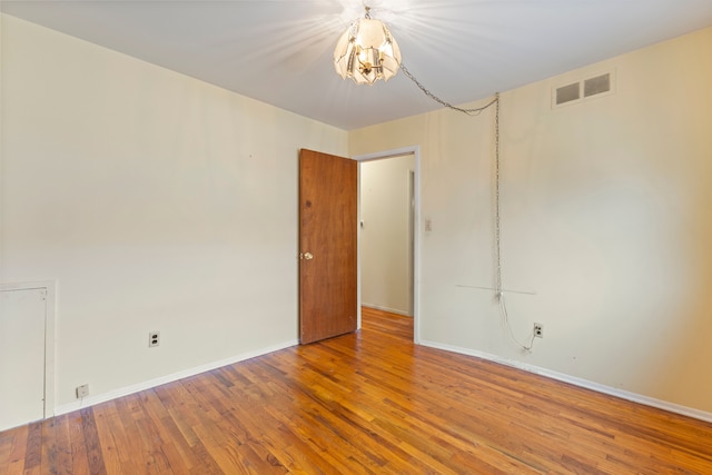 spare room featuring a chandelier, visible vents, wood finished floors, and baseboards