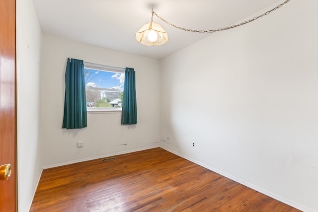 spare room featuring wood finished floors, visible vents, and baseboards