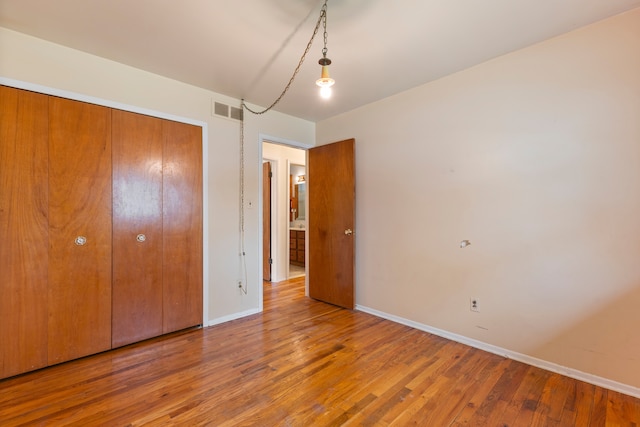 unfurnished bedroom featuring baseboards, visible vents, wood finished floors, and a closet