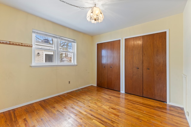 unfurnished bedroom with wood-type flooring, an inviting chandelier, multiple closets, and baseboards
