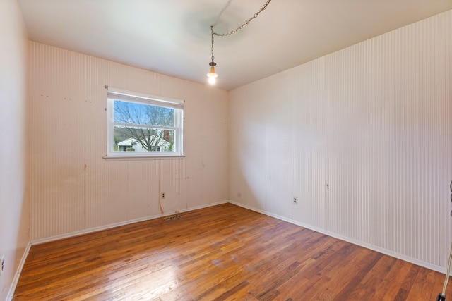 spare room with wood-type flooring, visible vents, and baseboards