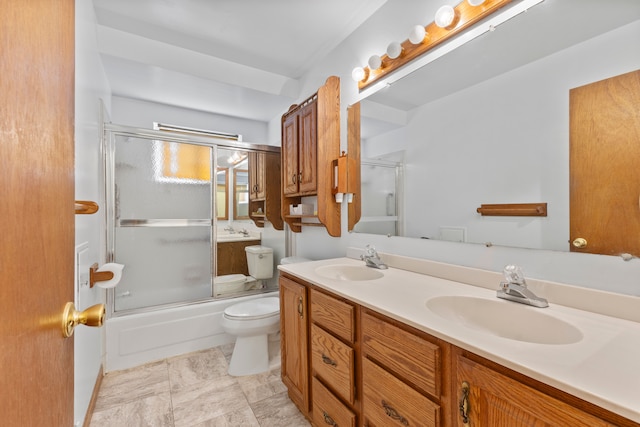 full bath with toilet, double vanity, a sink, and shower / bath combination with glass door