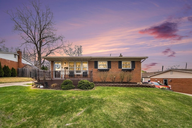 back of property at dusk with brick siding, a porch, and a yard