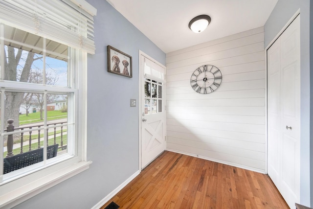 doorway to outside featuring baseboards, wood walls, light wood-style flooring, and plenty of natural light