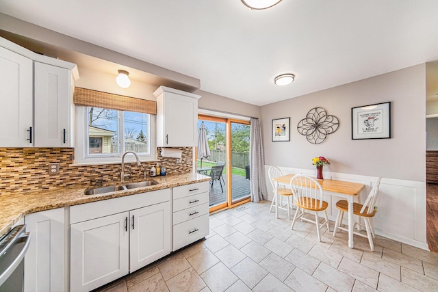 kitchen with tasteful backsplash, light stone counters, a sink, dishwasher, and white cabinets