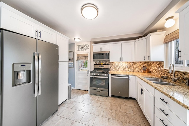 kitchen with a sink, tasteful backsplash, white cabinetry, light stone counters, and appliances with stainless steel finishes