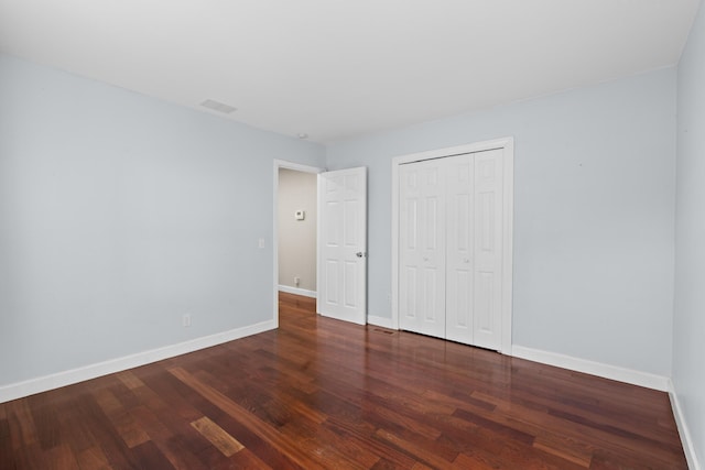 unfurnished bedroom featuring baseboards, wood finished floors, visible vents, and a closet