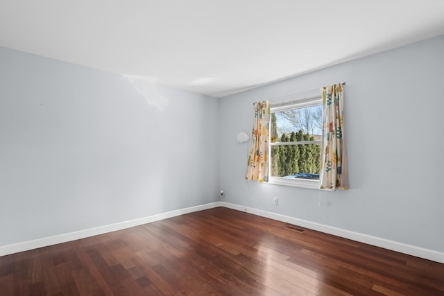 spare room featuring dark wood-type flooring, visible vents, and baseboards