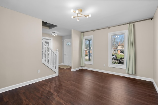 spare room featuring wood finished floors, visible vents, baseboards, a chandelier, and stairs