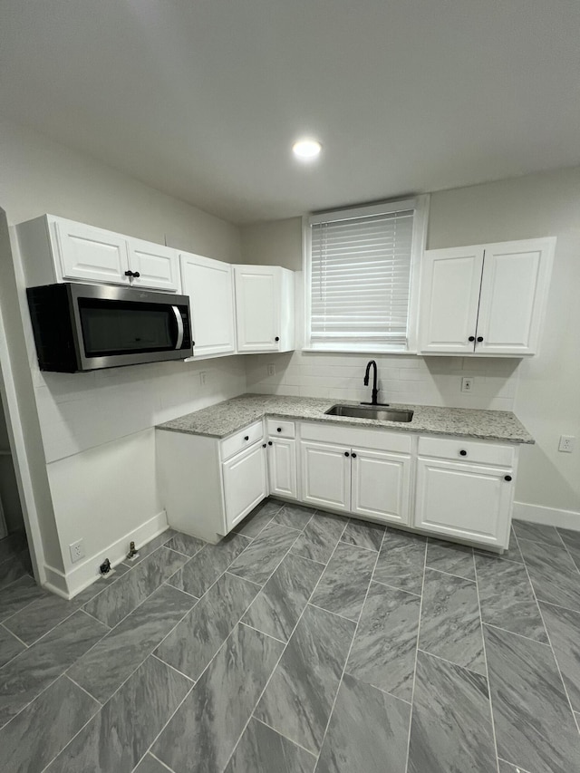 kitchen with white cabinets, a sink, stainless steel microwave, baseboards, and light stone counters
