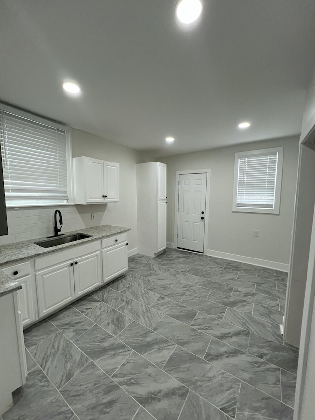 kitchen featuring a sink, baseboards, recessed lighting, white cabinetry, and light stone countertops