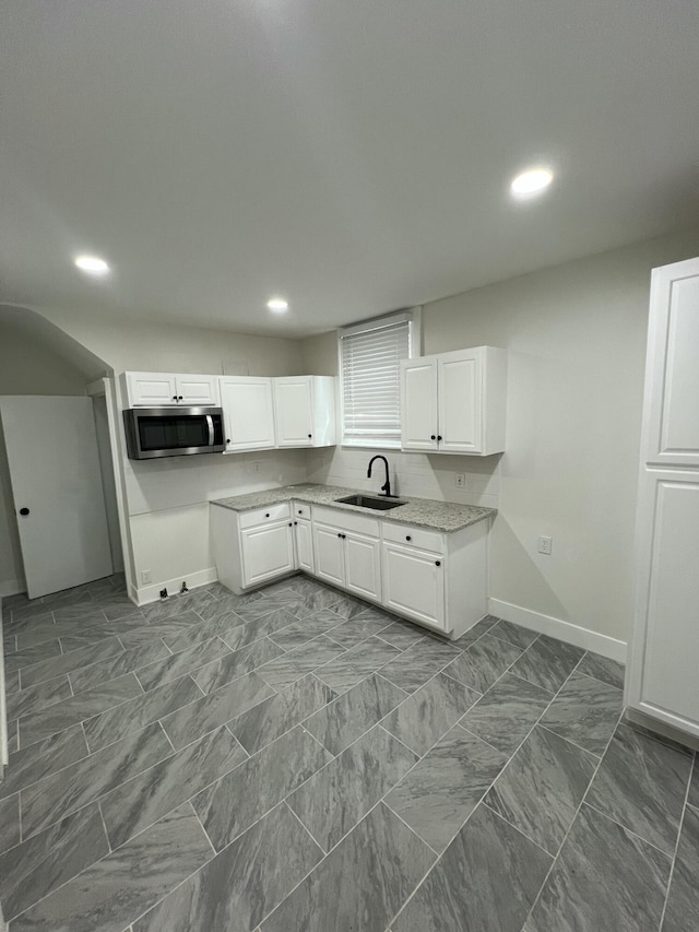kitchen featuring a sink, stainless steel microwave, baseboards, recessed lighting, and white cabinetry