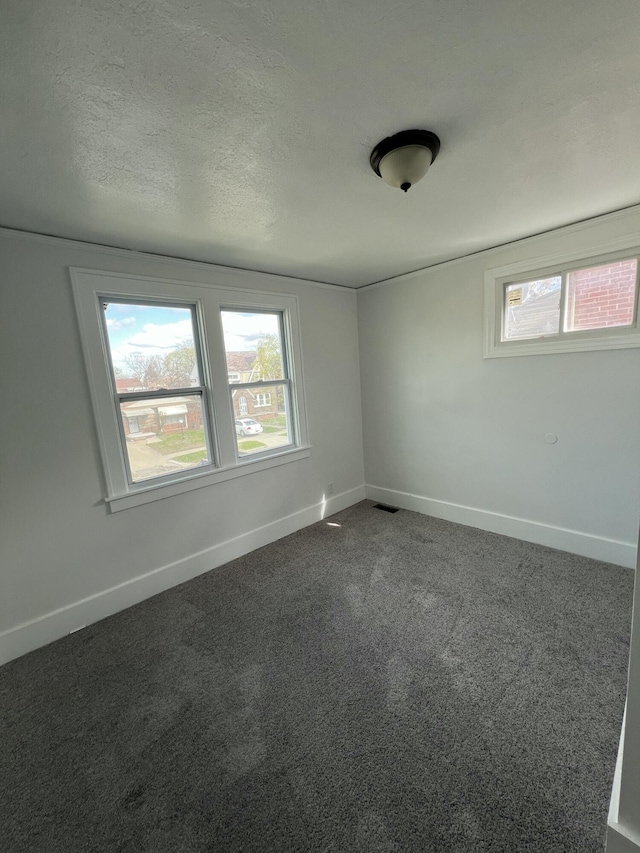 empty room with dark colored carpet, a healthy amount of sunlight, baseboards, and visible vents